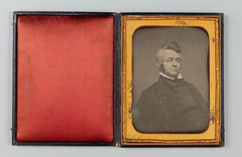 an opened photo album with a red felt lining on the left and a black and white photo of a man in 19th century attire