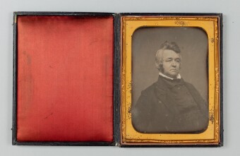 an opened photo album with a red felt lining on the left and a black and white photo of a man in 19th century attire
